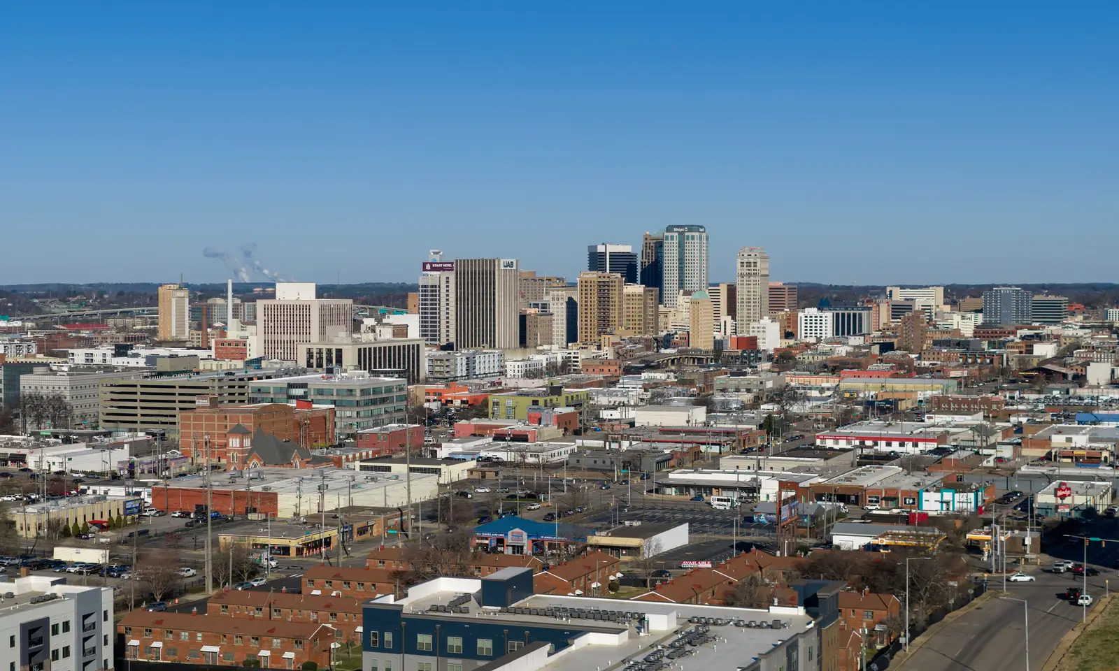 Aerial view of the downtown Birmingham, Alabama skyline on a clear day, showing high-rise office towers amid the city's urban core