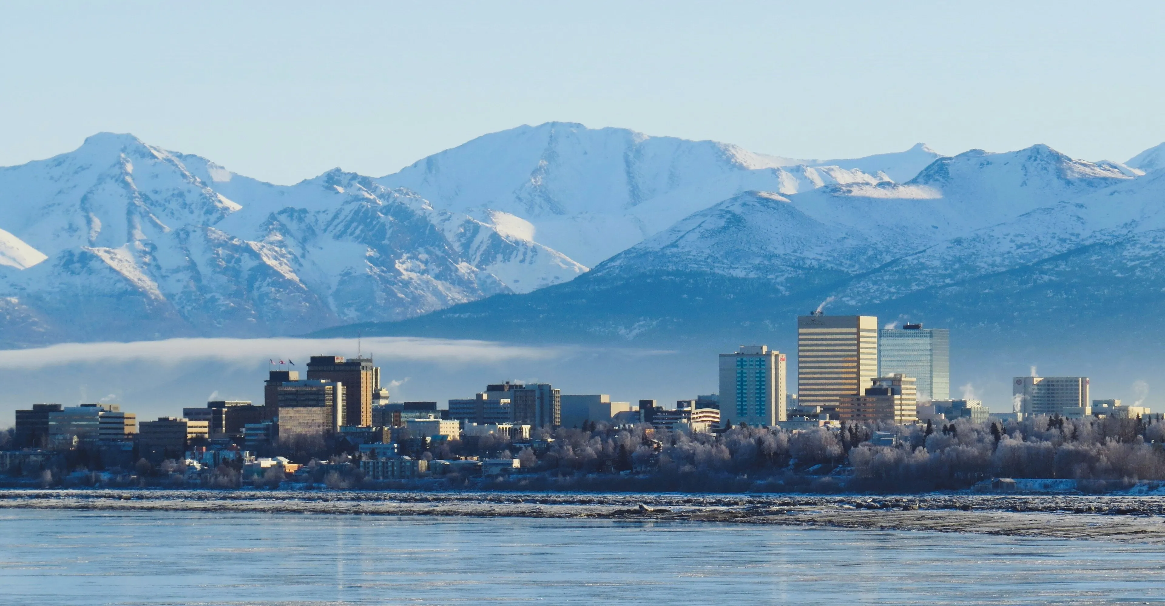 Downtown Anchorage, Alaska skyline in winter, snow-covered high-rises backed by the snow-capped Chugach Mountains with the frozen Cook Inlet in the foreground