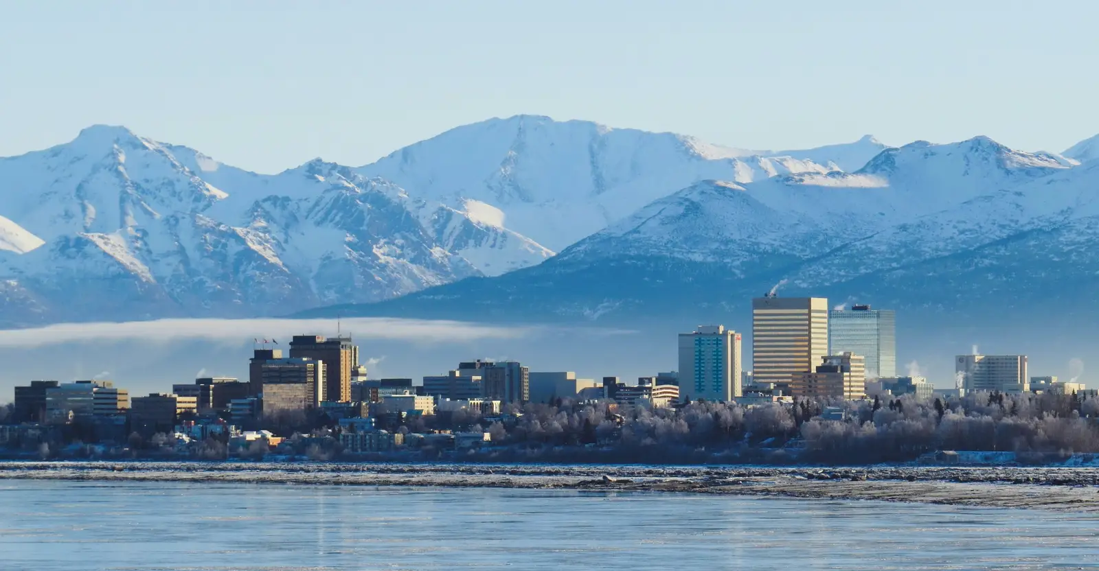 Downtown Anchorage, Alaska skyline in winter, snow-covered high-rises backed by the snow-capped Chugach Mountains with the frozen Cook Inlet in the foreground