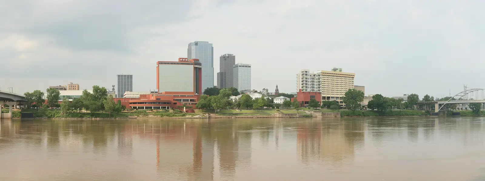 Wide panoramic view of the Little Rock, Arkansas skyline reflected across the Arkansas River, with downtown high-rise buildings