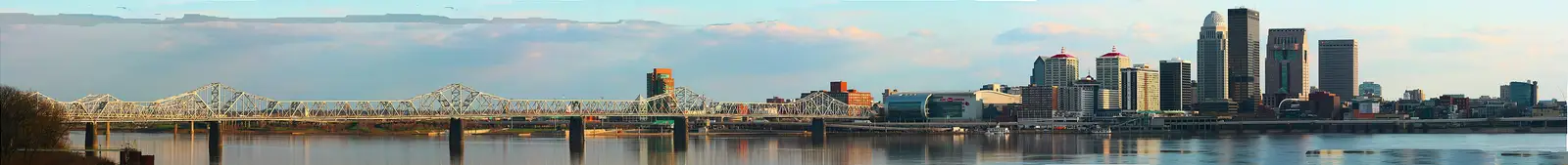 Wide daytime panorama of the Louisville, Kentucky skyline along the Ohio River, showing downtown high-rises and the KFC Yum! Center
