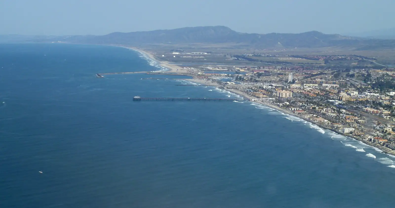 Aerial view of the Oceanside Pier stretching into the Pacific, with the beachfront and harbor beyond